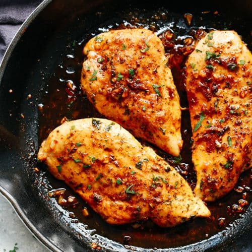 Three seasoned and cooked chicken breasts in a black skillet, garnished with herbs.