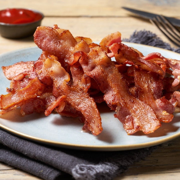 A plate of crispy, golden-brown bacon strips, with a small dish of ketchup.